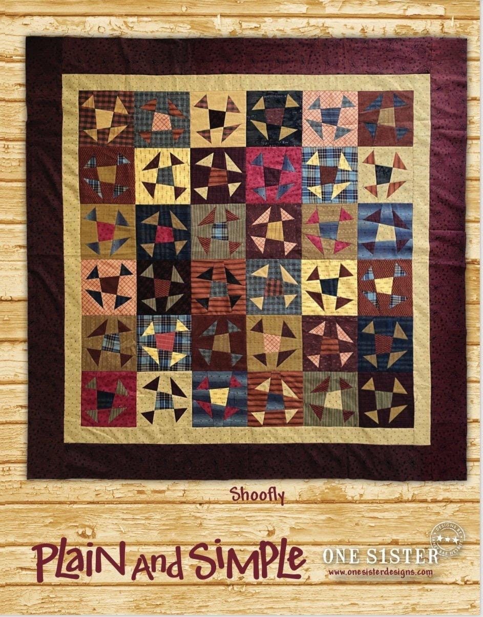 May include: Shoofly quilt pattern from One Sister Designs. This quilt features a patchwork design with various shades of brown, beige, and blue fabrics. The blocks are arranged in a grid pattern, creating a visually appealing design. The quilt is bordered with a darker brown fabric. The text 'Plain and Simple' is displayed below the quilt image, along with the company logo and website address.