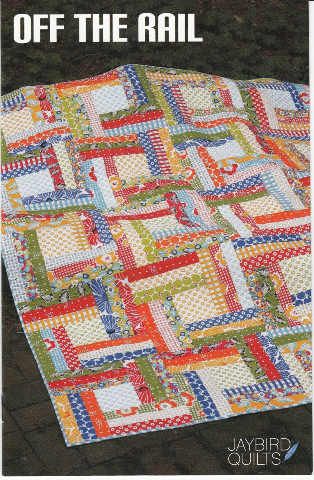 May include: A quilt with a log cabin pattern in red, orange, yellow, green, blue, and white fabrics. The quilt is on a brown surface. The text 'OFF THE RAIL' is at the top of the image. The text 'JAYBIRD QUILTS' is at the bottom of the image.