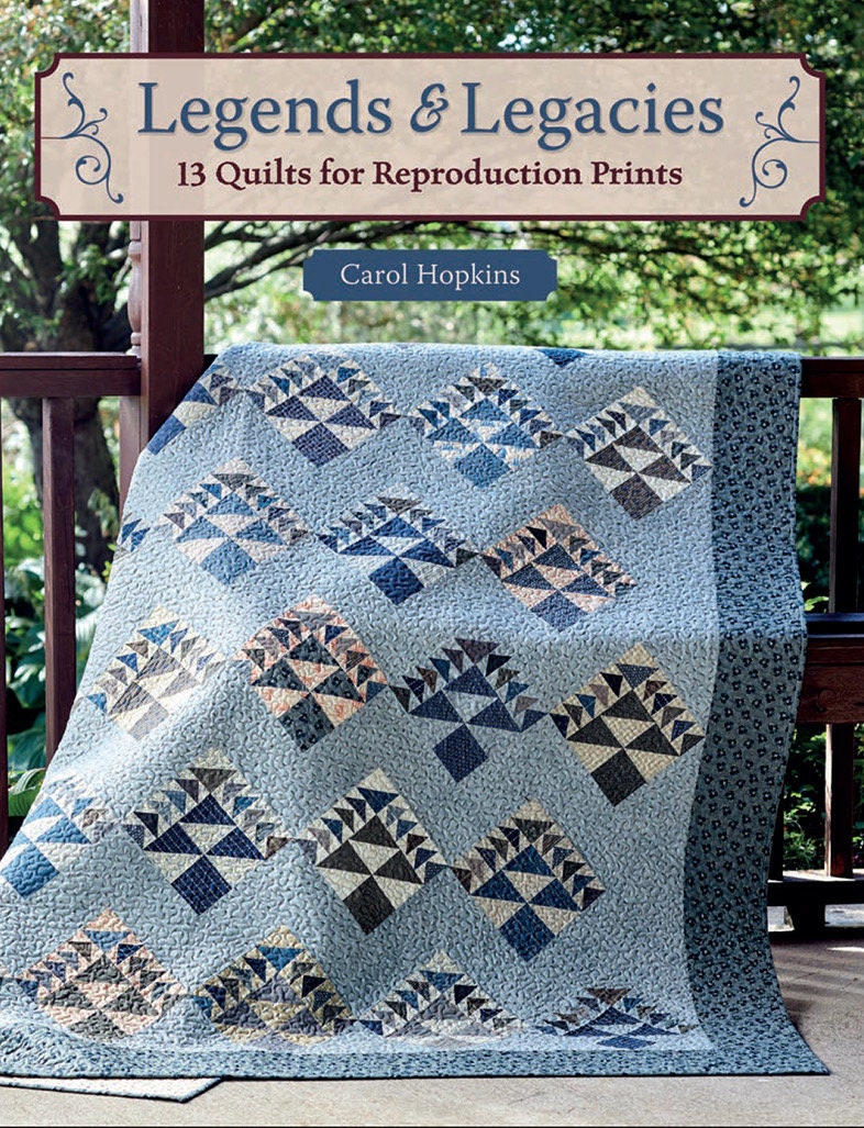 May include: A blue and white quilt with a geometric pattern. The quilt is folded and sitting on a wooden porch. The title "Legends & Legacies 13 Quilts for Reproduction Prints" is displayed above the quilt. The author's name, "Carol Hopkins", is displayed below the quilt.