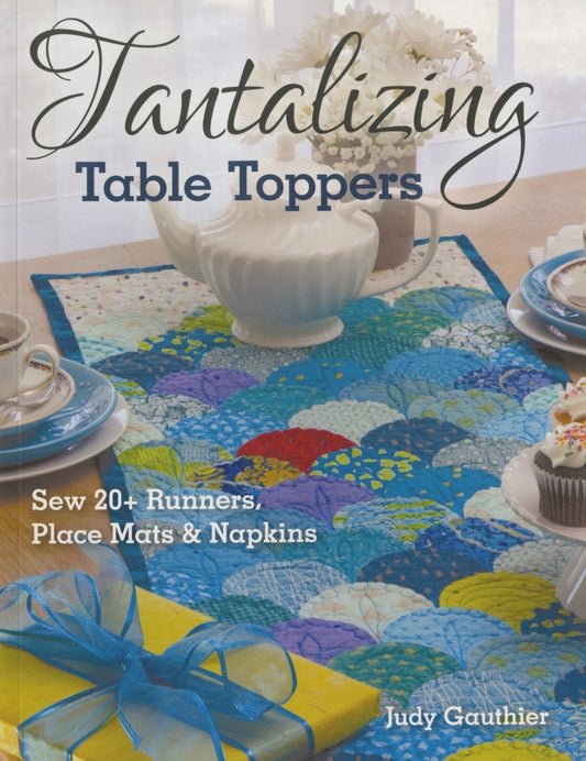 May include: A book titled "Tantalizing Table Toppers" with a blue, yellow, and purple quilted table runner on the cover. The book features instructions for sewing over 20 table runners, place mats, and napkins.
