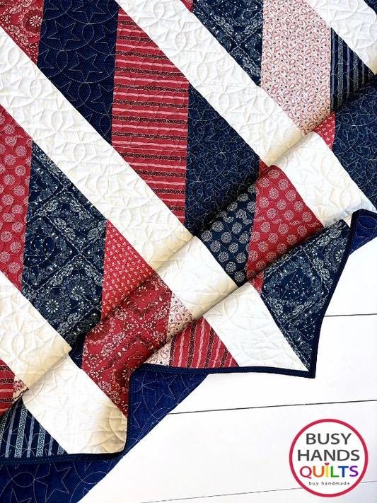 May include: A red, white, and blue chevron quilt with a star pattern quilted into the white fabric. The quilt is folded in half and the fabric is made of cotton. The quilt is handmade by Busy Hands Quilts.